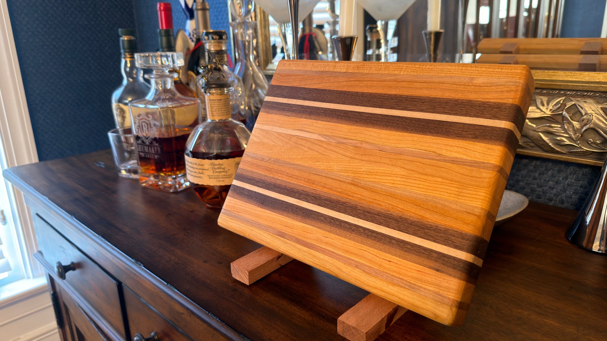 Multi-species edge-grain cutting board — walnut, cherry, and maple stripes on display stand